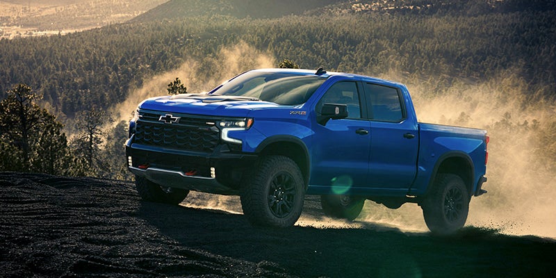 Blue Chevrolet truck driving on dirt trail in forest
