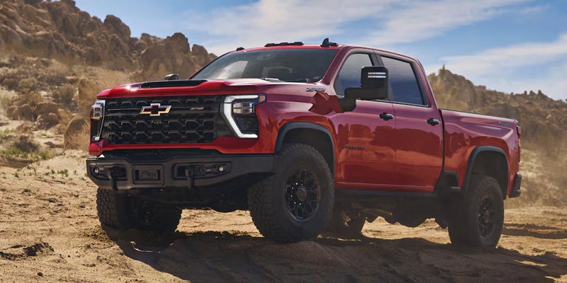 Red Chevrolet Silverado HD ZR2 pickup truck driving on a rocky, dirt path