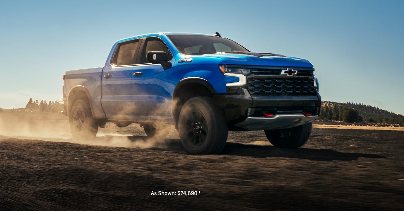 Blue Chevrolet Silverado driving off-road, kicking up dirt.