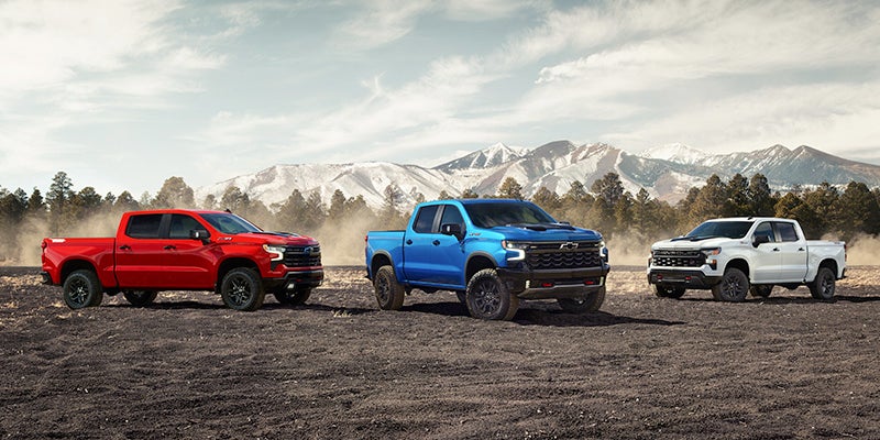 Red, blue, and white Chevrolet trucks on rugged terrain